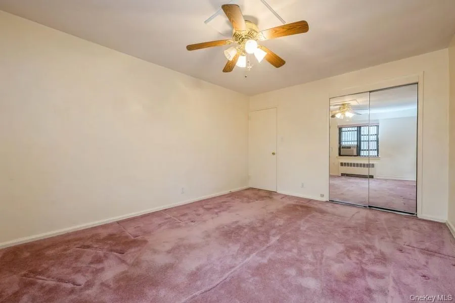 Unfurnished bedroom with carpet flooring, radiator heating unit, a ceiling fan, a closet, and cooling unit Unfurnished bedroom with carpet flooring, radiator heating unit, a ceiling fan, a closet, and cooling unit