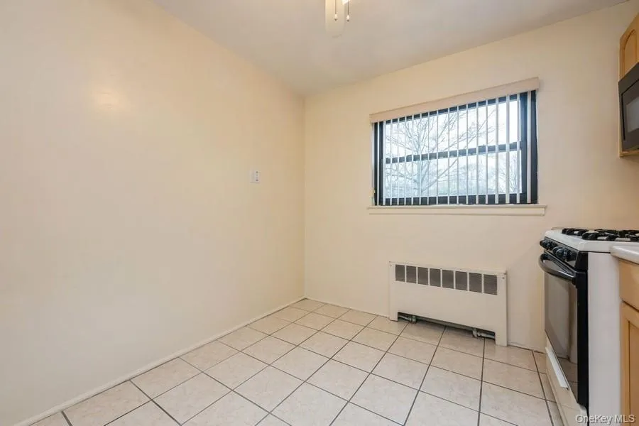 Kitchen with radiator heating unit, white gas range, light tile patterned floors, black microwave, and a ceiling fan Kitchen with radiator heating unit, white gas range, light tile patterned floors, black microwave, and a ceiling fan