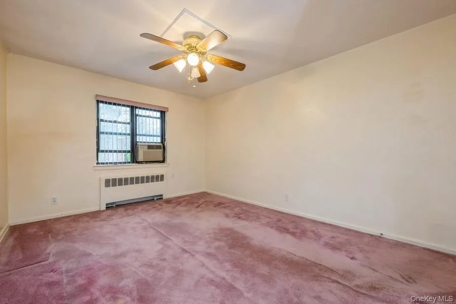 Carpeted spare room featuring radiator heating unit and a ceiling fan Carpeted spare room featuring radiator heating unit and a ceiling fan