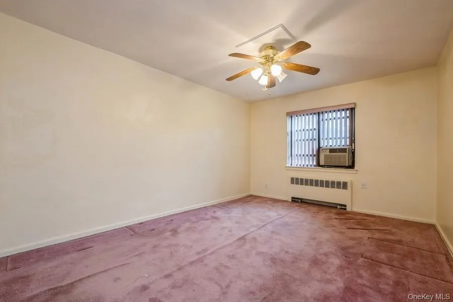 Carpeted spare room featuring radiator, ceiling fan, and cooling unit Carpeted spare room featuring radiator, ceiling fan, and cooling unit