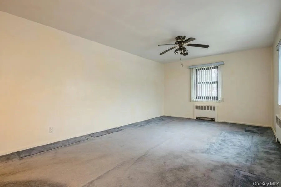 Unfurnished room with carpet floors, radiator heating unit, and ceiling fan Unfurnished room with carpet floors, radiator heating unit, and ceiling fan