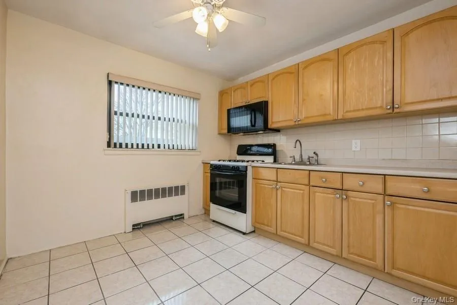 Kitchen with white gas range, light countertops, backsplash, radiator, and black microwave Kitchen with white gas range, light countertops, backsplash, radiator, and black microwave