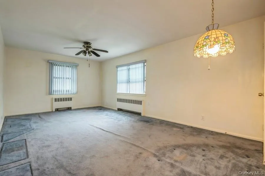 Spare room featuring radiator heating unit, carpet, and a ceiling fan Spare room featuring radiator heating unit, carpet, and a ceiling fan