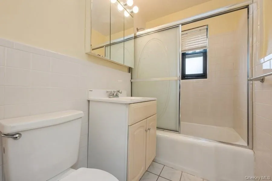 Bathroom featuring enclosed tub / shower combo, tile walls, vanity, and light tile patterned floors Bathroom featuring enclosed tub / shower combo, tile walls, vanity, and light tile patterned floors