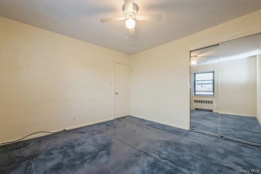 Unfurnished bedroom featuring a ceiling fan, radiator, carpet flooring, and a closet Unfurnished bedroom featuring a ceiling fan, radiator, carpet flooring, and a closet