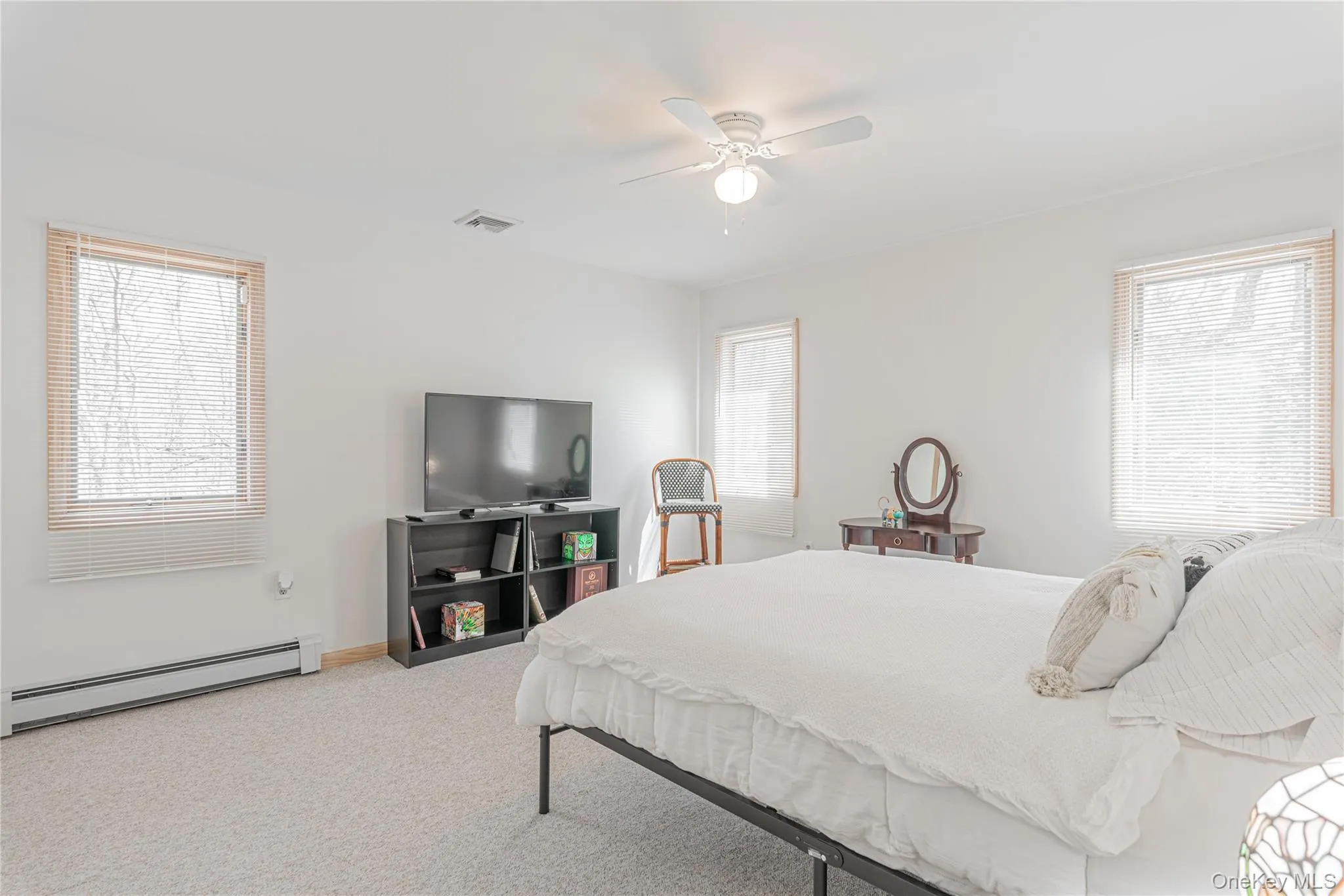 Bedroom featuring a baseboard radiator, light colored carpet, multiple windows, and ceiling fan Bedroom featuring a baseboard radiator, light colored carpet, multiple windows, and ceiling fan
