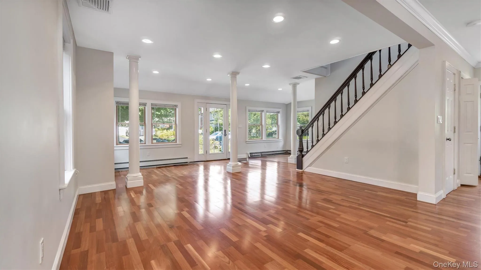 Unfurnished living room featuring stairway, ornate columns, light wood-style flooring, recessed lighting, and a baseboard radiator Unfurnished living room featuring stairway, ornate columns, light wood-style flooring, recessed lighting, and a baseboard radiator