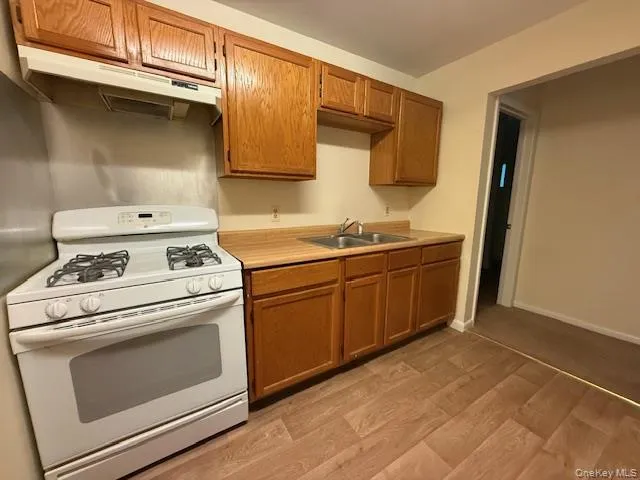 Kitchen with white gas stove, under cabinet range hood, light wood finished floors, and light countertops Kitchen with white gas stove, under cabinet range hood, light wood finished floors, and light countertops