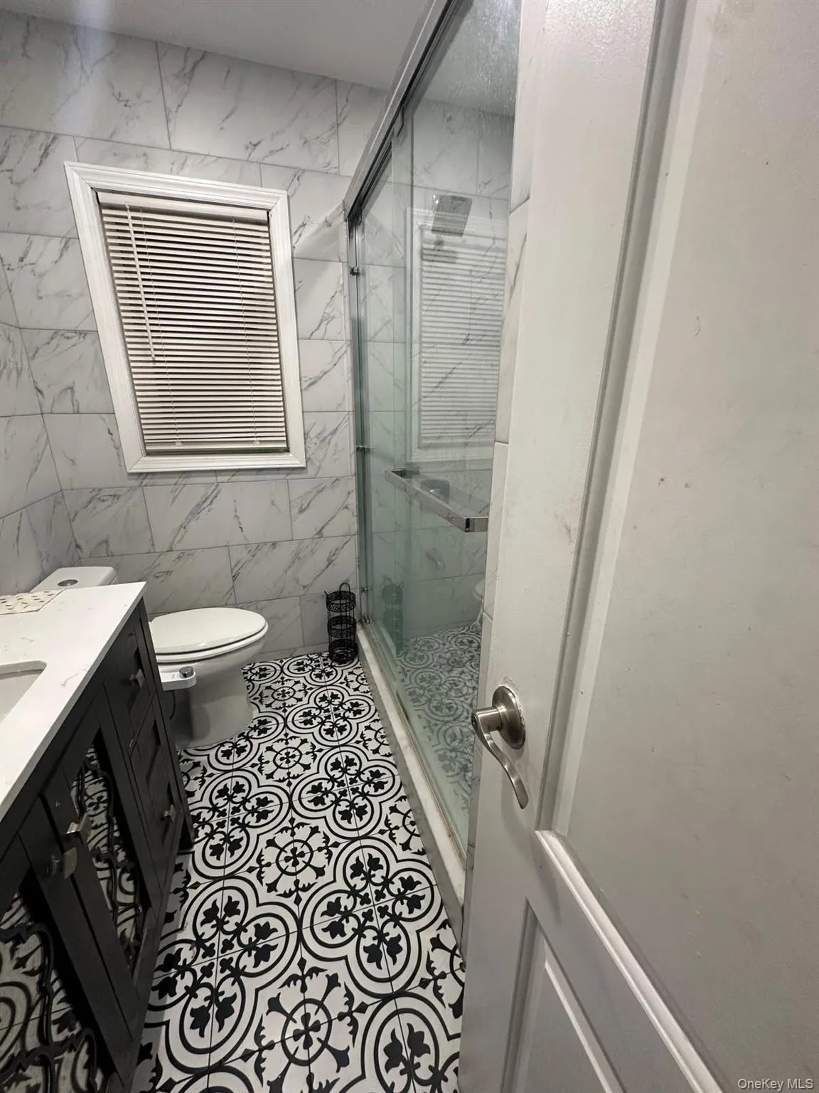 Bathroom featuring tile walls, vanity, a marble finish shower, and tile patterned flooring Bathroom featuring tile walls, vanity, a marble finish shower, and tile patterned flooring