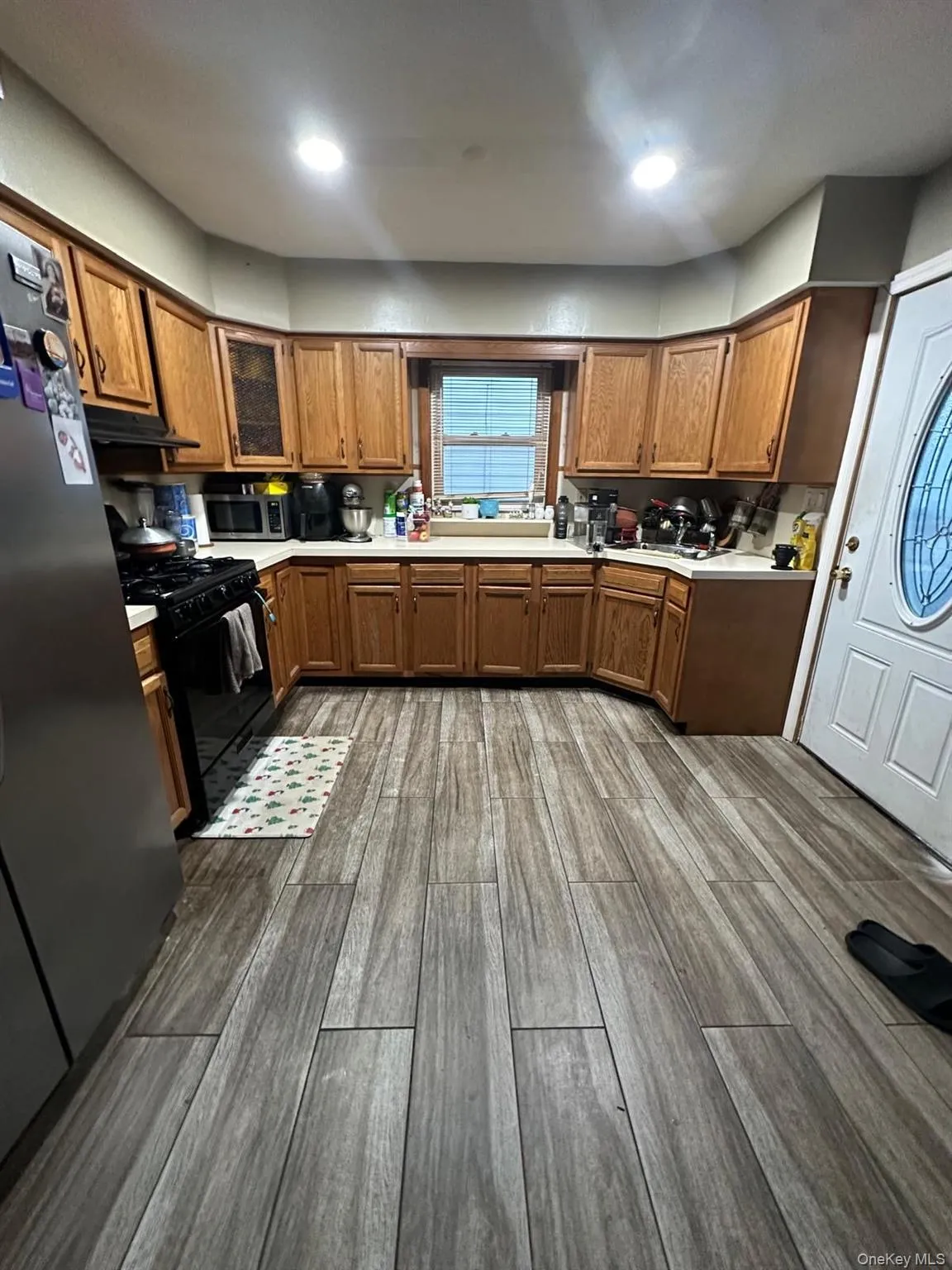 Kitchen featuring brown cabinetry, dark wood-style flooring, stainless steel appliances, light countertops, and recessed lighting Kitchen featuring brown cabinetry, dark wood-style flooring, stainless steel appliances, light countertops, and recessed lighting