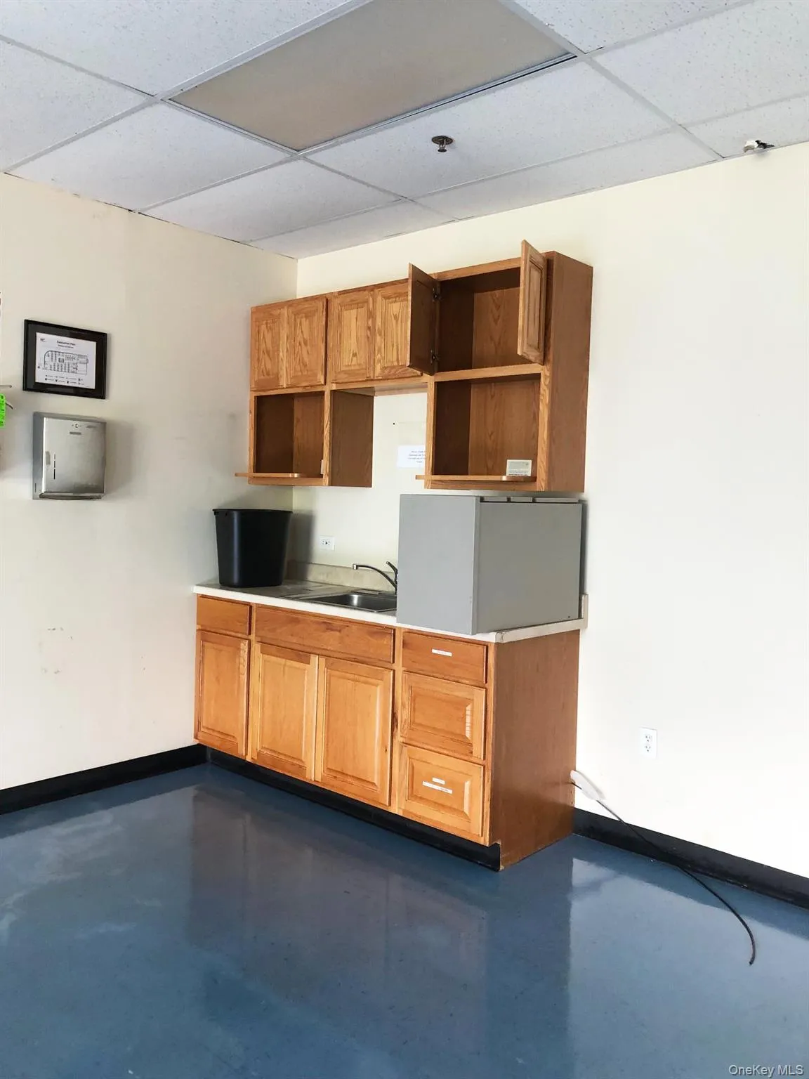 Kitchen featuring a paneled ceiling, finished concrete floors, brown cabinetry, and light countertops Kitchen featuring a paneled ceiling, finished concrete floors, brown cabinetry, and light countertops