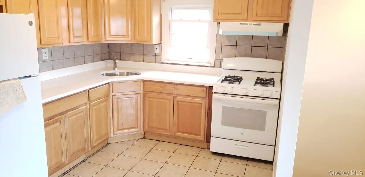 Kitchen featuring white appliances, light brown cabinets, light countertops, under cabinet range hood, and light tile patterned floors Kitchen featuring white appliances, light brown cabinets, light countertops, under cabinet range hood, and light tile patterned floors