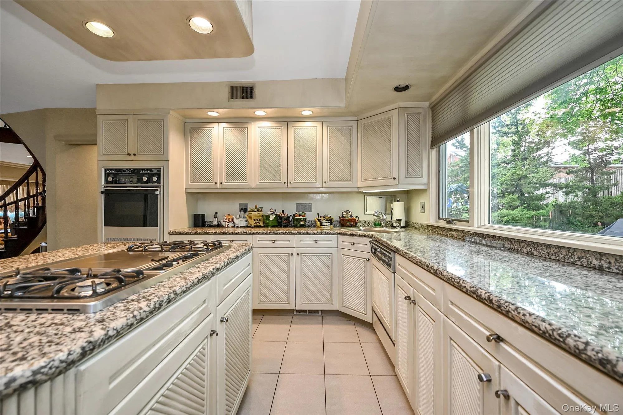 Kitchen with light stone countertops, recessed lighting, stainless steel gas cooktop, black oven, and light tile patterned floors Kitchen with light stone countertops, recessed lighting, stainless steel gas cooktop, black oven, and light tile patterned floors