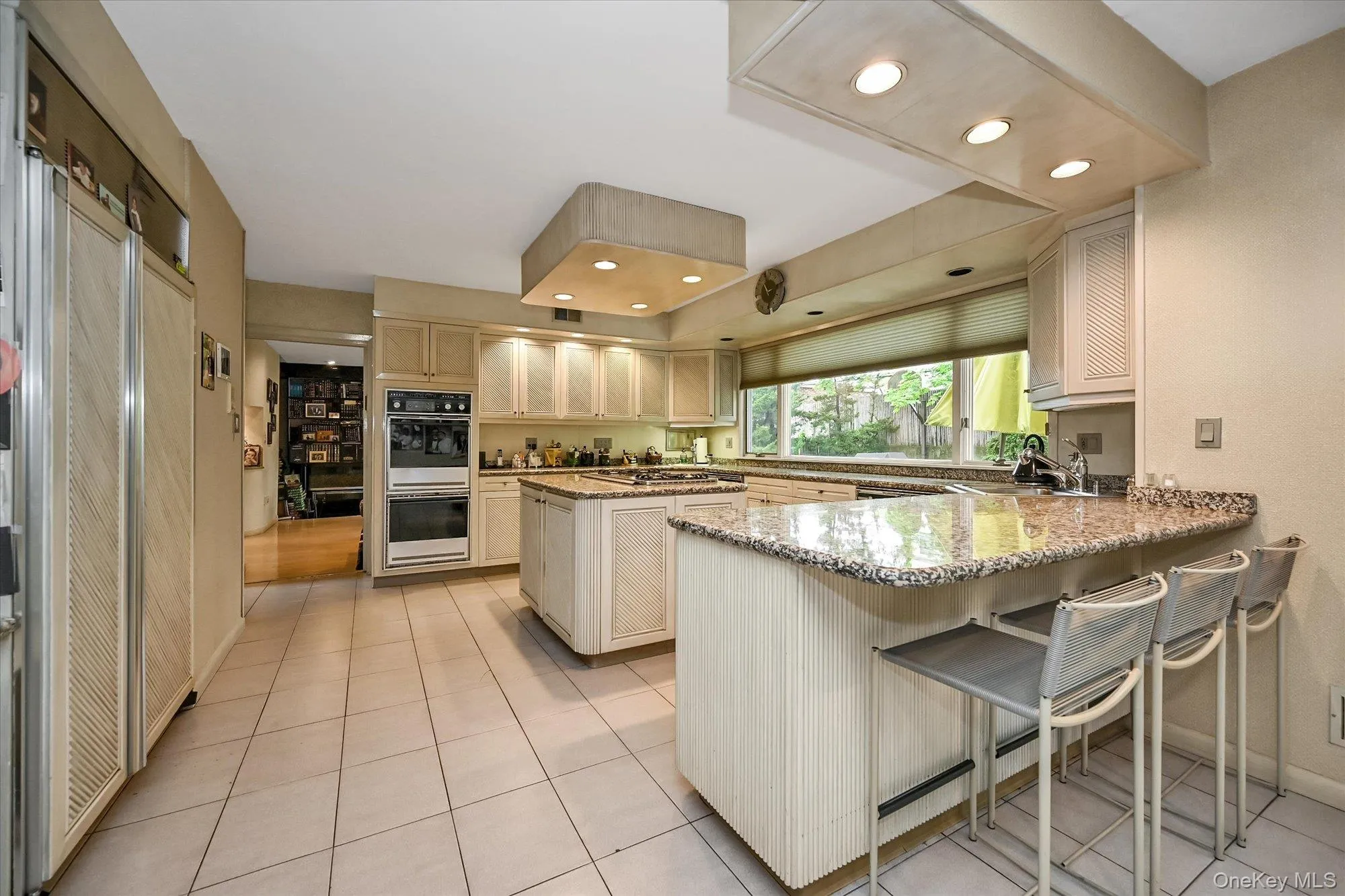 Kitchen with light tile patterned flooring, recessed lighting, a breakfast bar area, light stone counters, and a peninsula Kitchen with light tile patterned flooring, recessed lighting, a breakfast bar area, light stone counters, and a peninsula