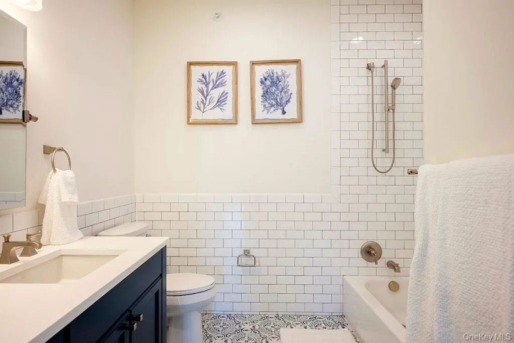 Bathroom with tile walls, shower / washtub combination, vanity, wainscoting, and light tile patterned flooring Bathroom with tile walls, shower / washtub combination, vanity, wainscoting, and light tile patterned flooring