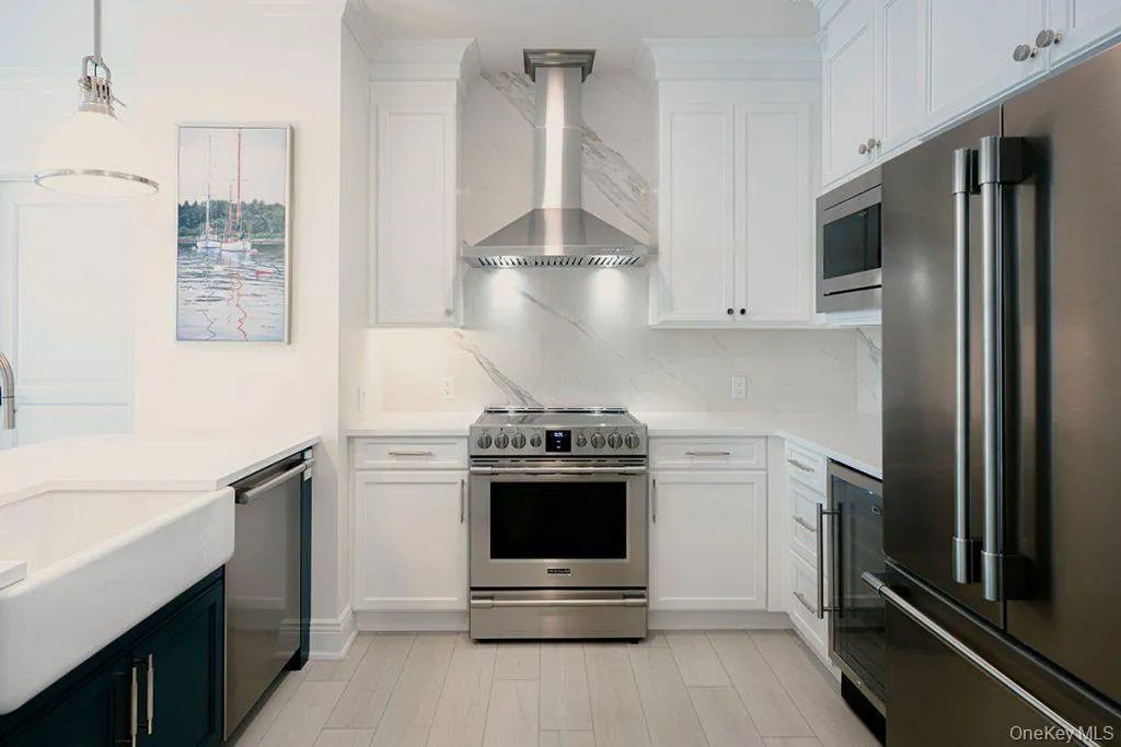 Kitchen with appliances with stainless steel finishes, wall chimney range hood, white cabinetry, and hanging light fixtures Kitchen with appliances with stainless steel finishes, wall chimney range hood, white cabinetry, and hanging light fixtures