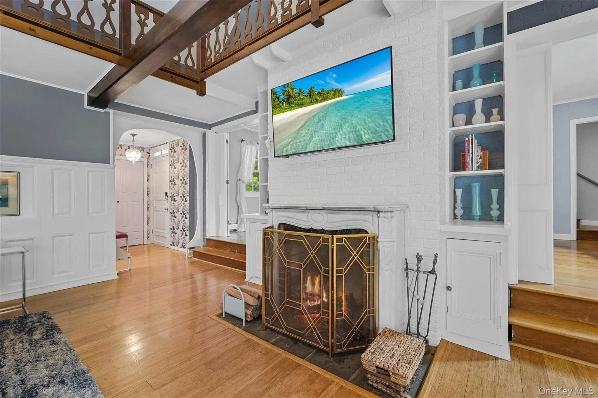 Living area featuring hardwood / wood-style flooring, arched walkways, a brick fireplace, a decorative wall, and ornamental molding Living area featuring hardwood / wood-style flooring, arched walkways, a brick fireplace, a decorative wall, and ornamental molding