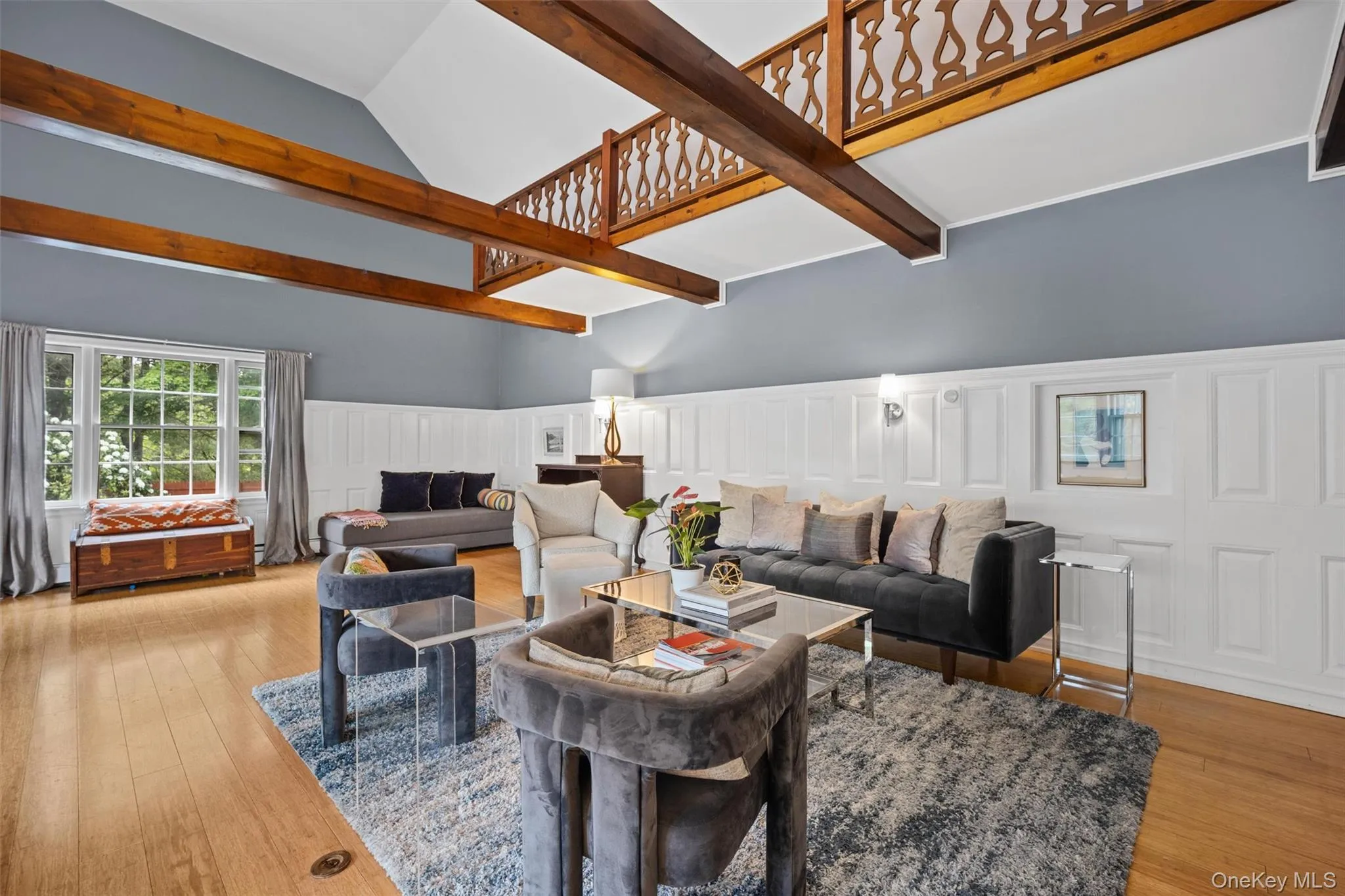 Living area with a decorative wall, hardwood / wood-style flooring, a wainscoted wall, a high ceiling, and beam ceiling Living area with a decorative wall, hardwood / wood-style flooring, a wainscoted wall, a high ceiling, and beam ceiling