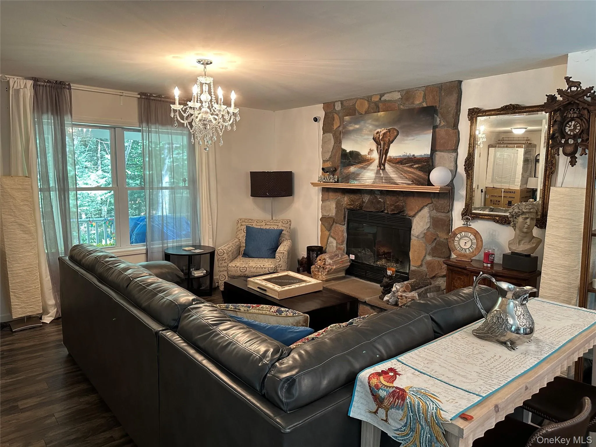 Living room with a stone fireplace, wood finished floors, and a chandelier Living room with a stone fireplace, wood finished floors, and a chandelier