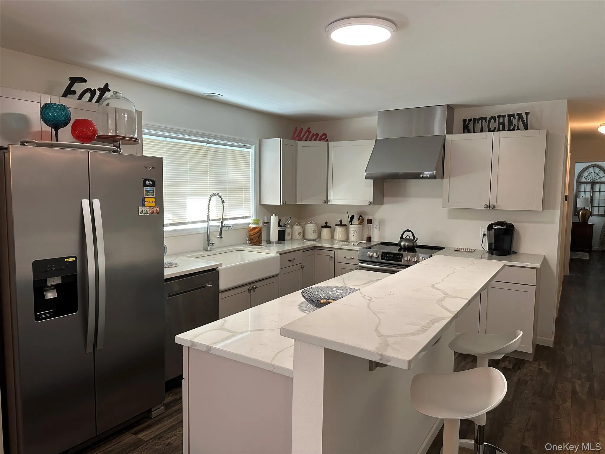 Kitchen featuring appliances with stainless steel finishes, light stone countertops, wall chimney range hood, dark wood-style floors, and a breakfast bar area Kitchen featuring appliances with stainless steel finishes, light stone countertops, wall chimney range hood, dark wood-style floors, and a breakfast bar area