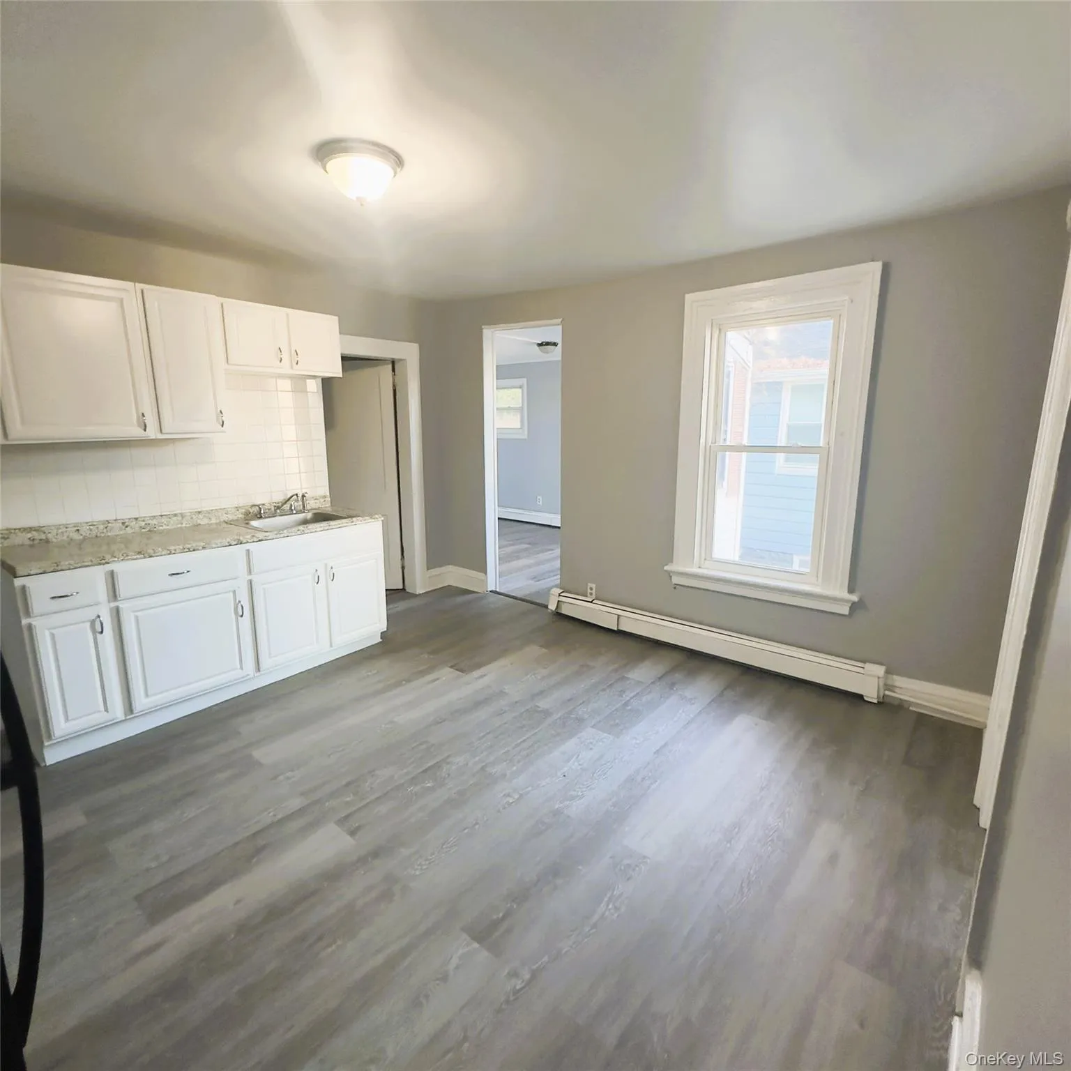Kitchen with decorative backsplash, light countertops, a baseboard heating unit, white cabinetry, and light vinyl flooring Kitchen with decorative backsplash, light countertops, a baseboard heating unit, white cabinetry, and light vinyl flooring