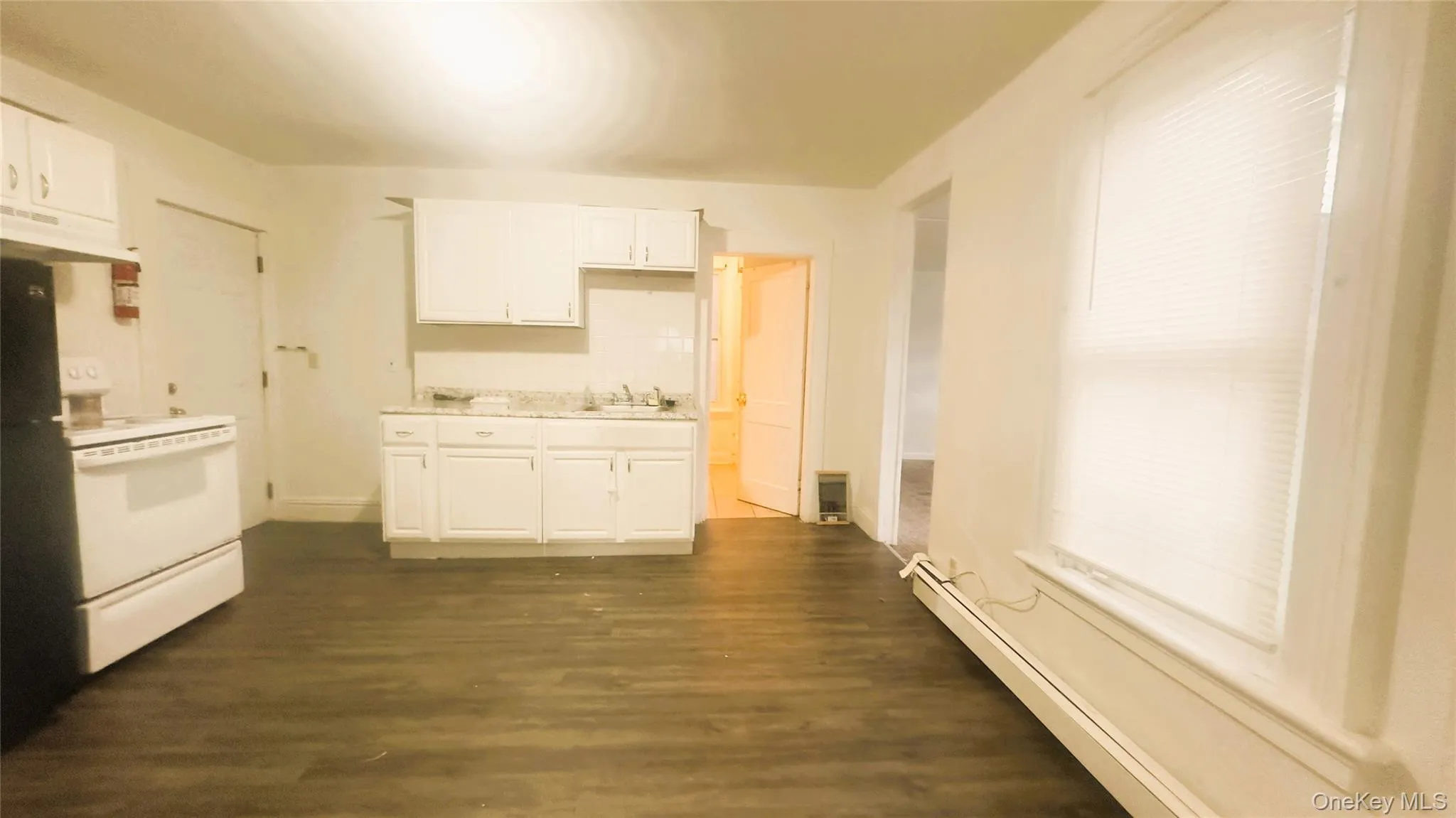 Kitchen featuring white electric stove, baseboard heating, light countertops, and white cabinetry, vinyl flooring. Kitchen featuring white electric stove, baseboard heating, light countertops, and white cabinetry, vinyl flooring.