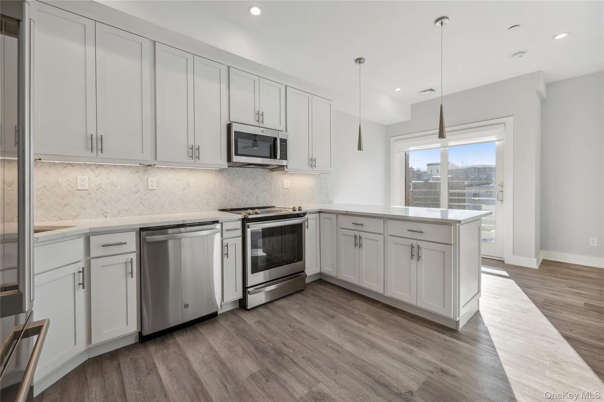 Kitchen featuring stainless steel appliances, white cabinetry, backsplash, pendant lighting, and a peninsula Kitchen featuring stainless steel appliances, white cabinetry, backsplash, pendant lighting, and a peninsula