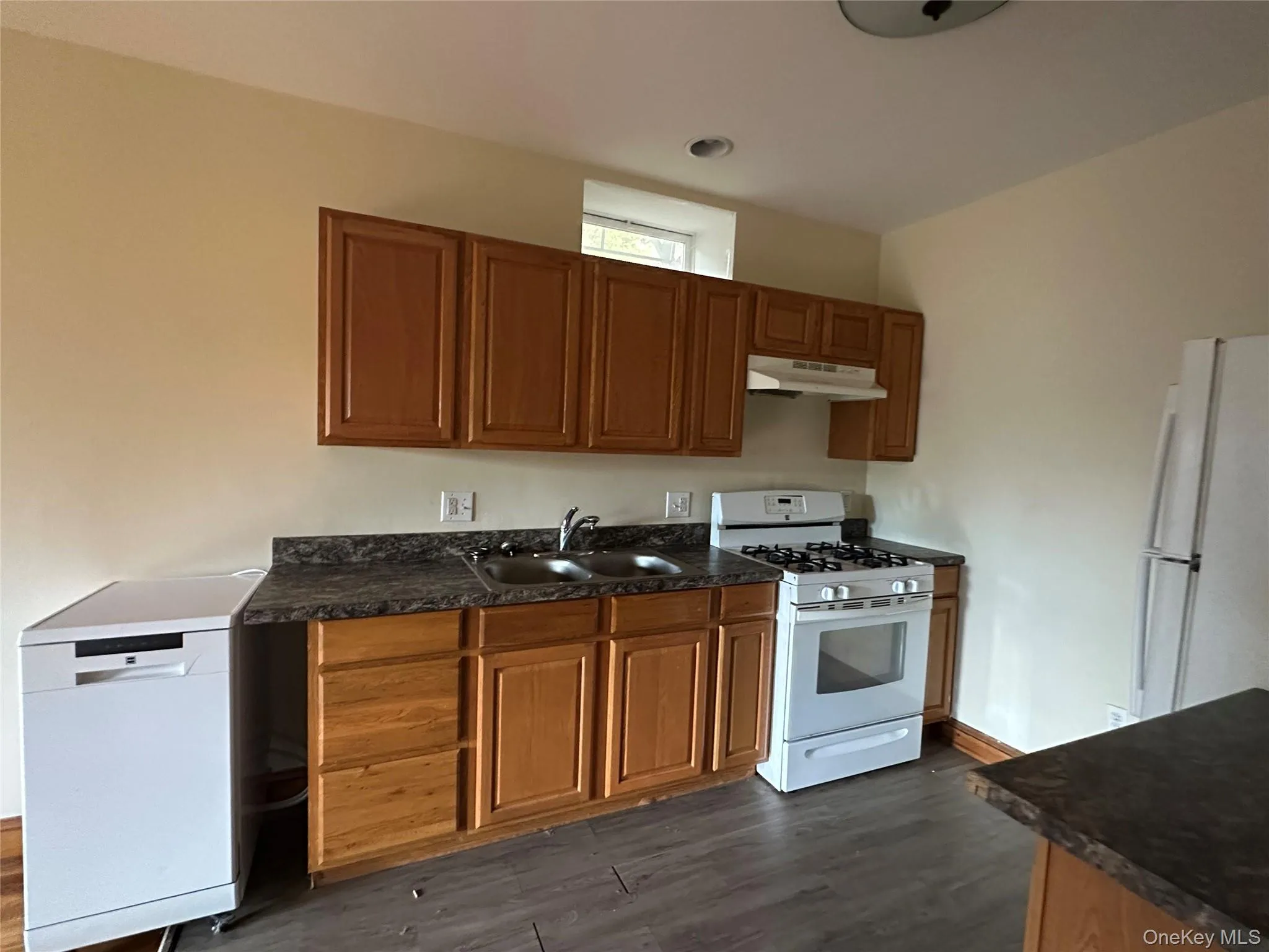 Kitchen featuring white appliances, dark countertops, and brown cabinetry Kitchen featuring white appliances, dark countertops, and brown cabinetry