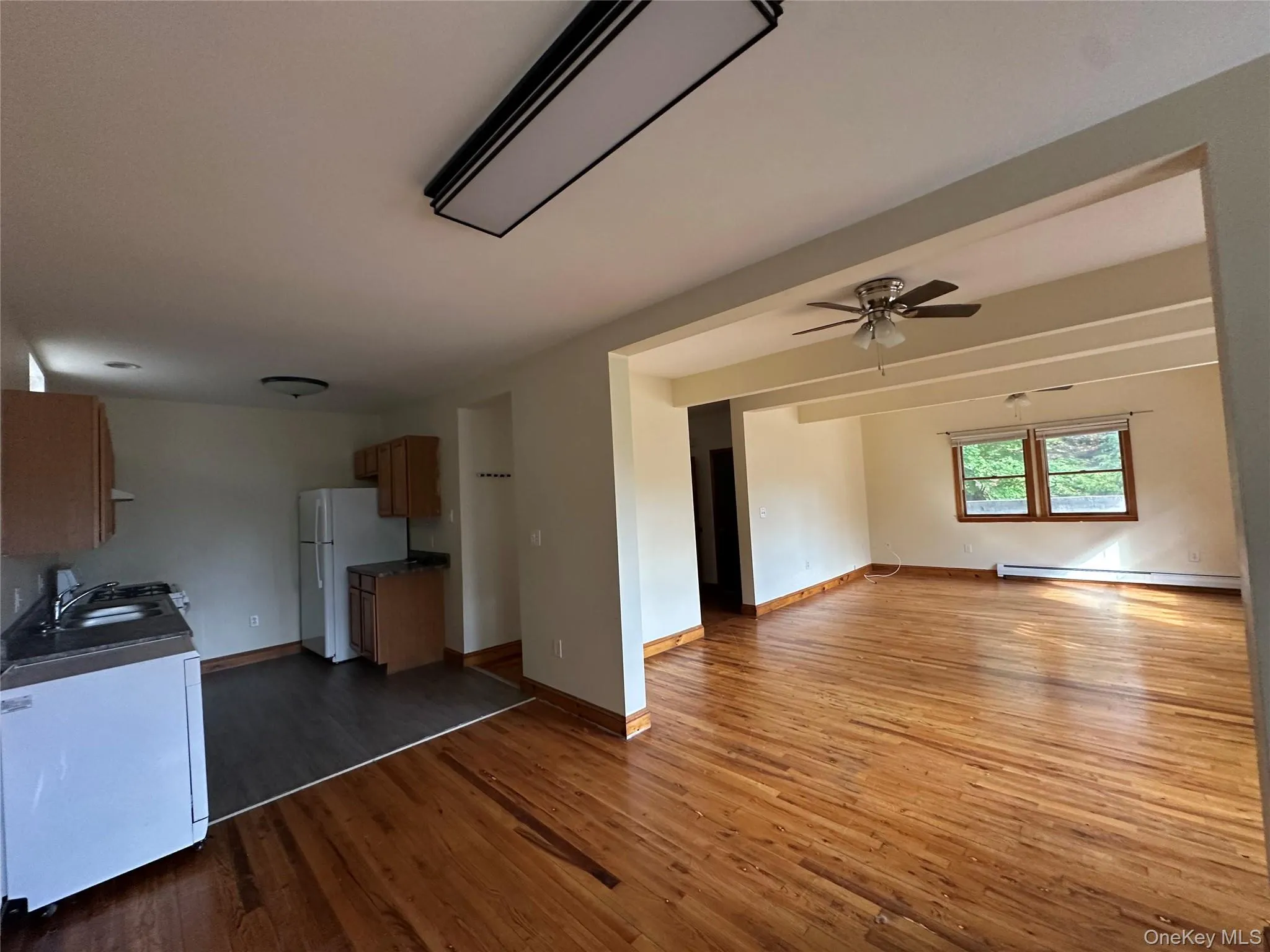 Unfurnished living room with dark wood-style flooring, a ceiling fan, and a baseboard heating unit Unfurnished living room with dark wood-style flooring, a ceiling fan, and a baseboard heating unit
