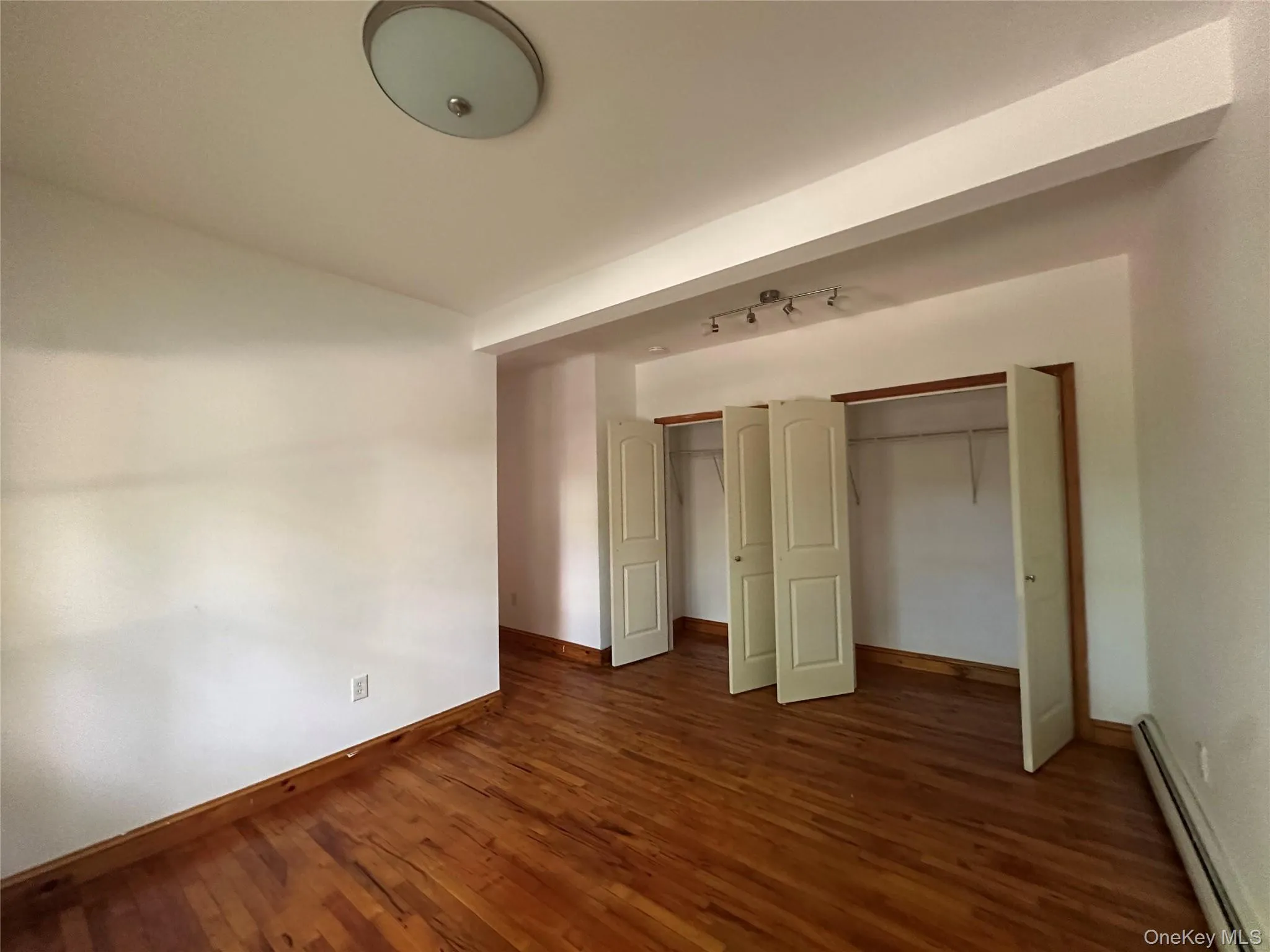 Unfurnished bedroom featuring a baseboard radiator, dark wood-style floors, a closet, and track lighting Unfurnished bedroom featuring a baseboard radiator, dark wood-style floors, a closet, and track lighting