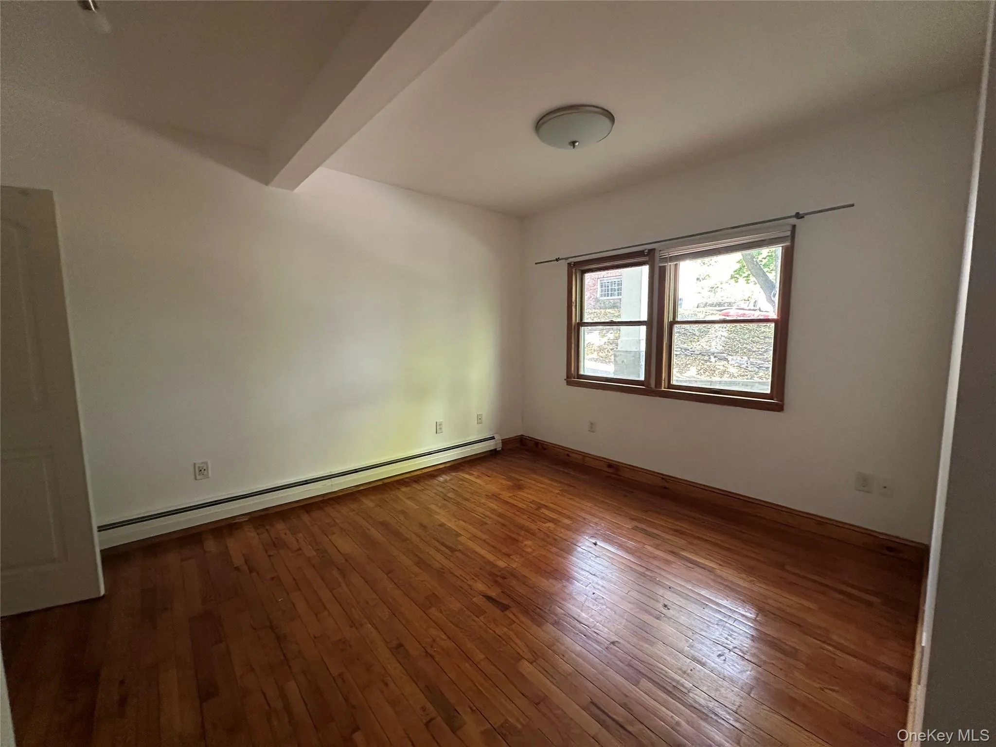 Empty room with baseboard heating, dark wood finished floors, and beamed ceiling Empty room with baseboard heating, dark wood finished floors, and beamed ceiling