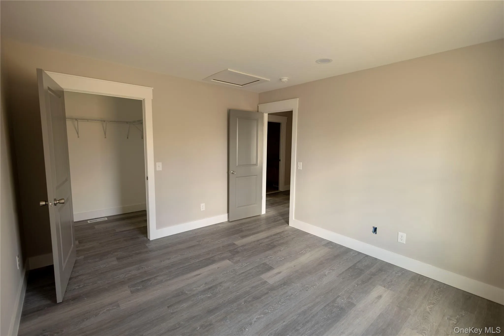 Unfurnished bedroom with attic access, wood finished floors, and a spacious closet Unfurnished bedroom with attic access, wood finished floors, and a spacious closet