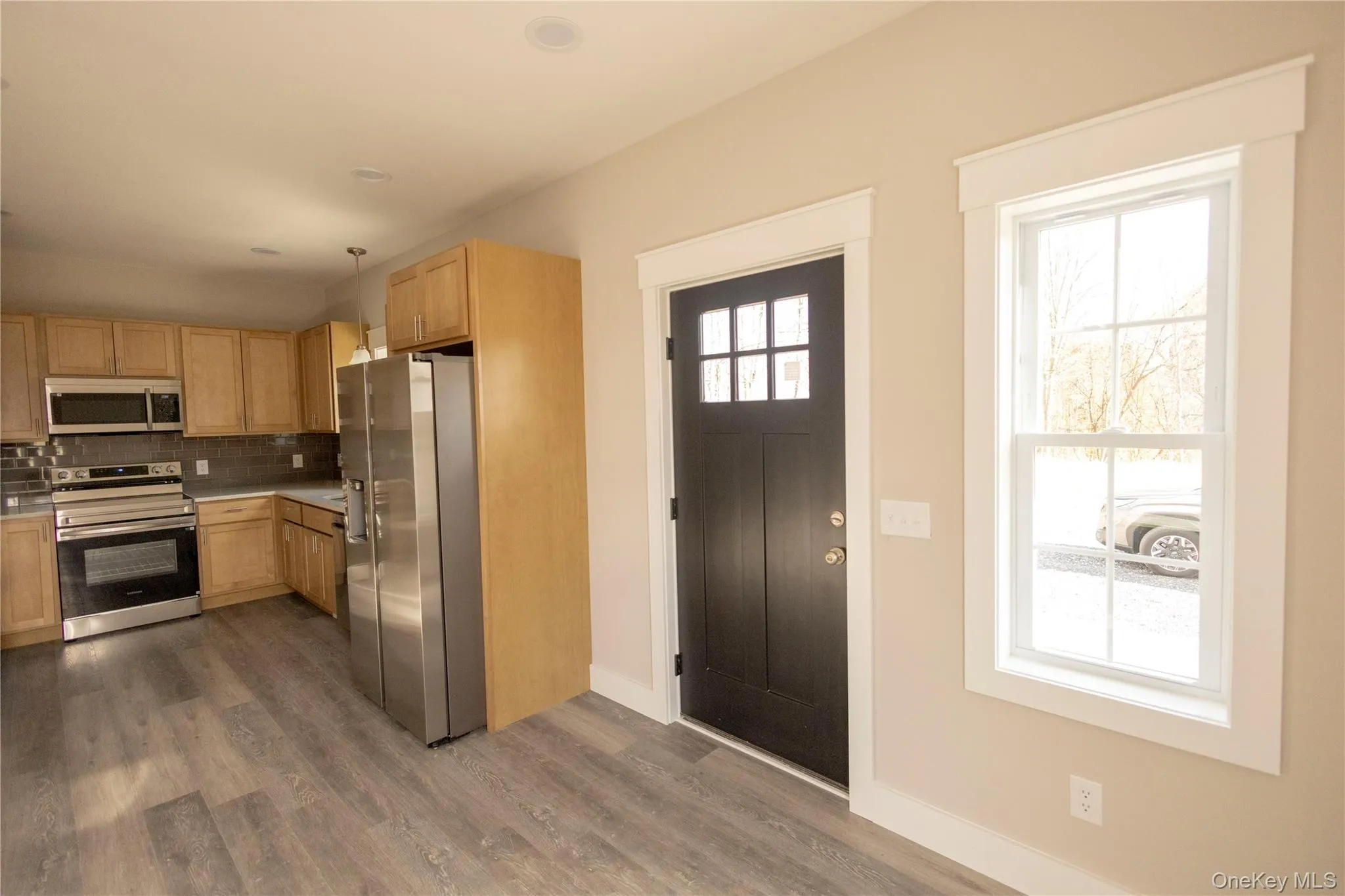 Kitchen featuring stainless steel appliances, light countertops, backsplash, dark wood finished floors, and light brown cabinets Kitchen featuring stainless steel appliances, light countertops, backsplash, dark wood finished floors, and light brown cabinets