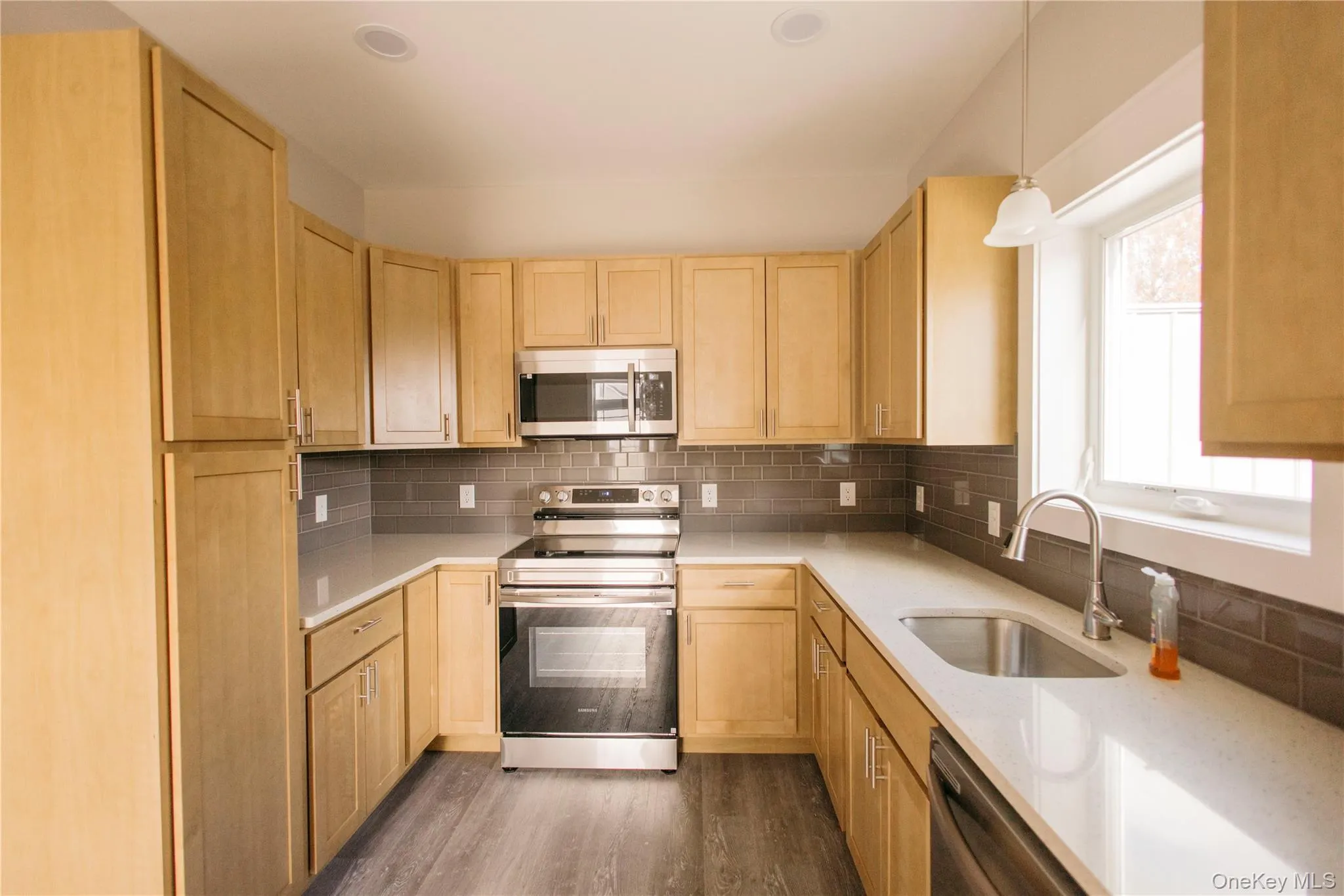 Kitchen featuring appliances with stainless steel finishes, light brown cabinetry, backsplash, dark wood-style flooring, and light stone countertops Kitchen featuring appliances with stainless steel finishes, light brown cabinetry, backsplash, dark wood-style flooring, and light stone countertops