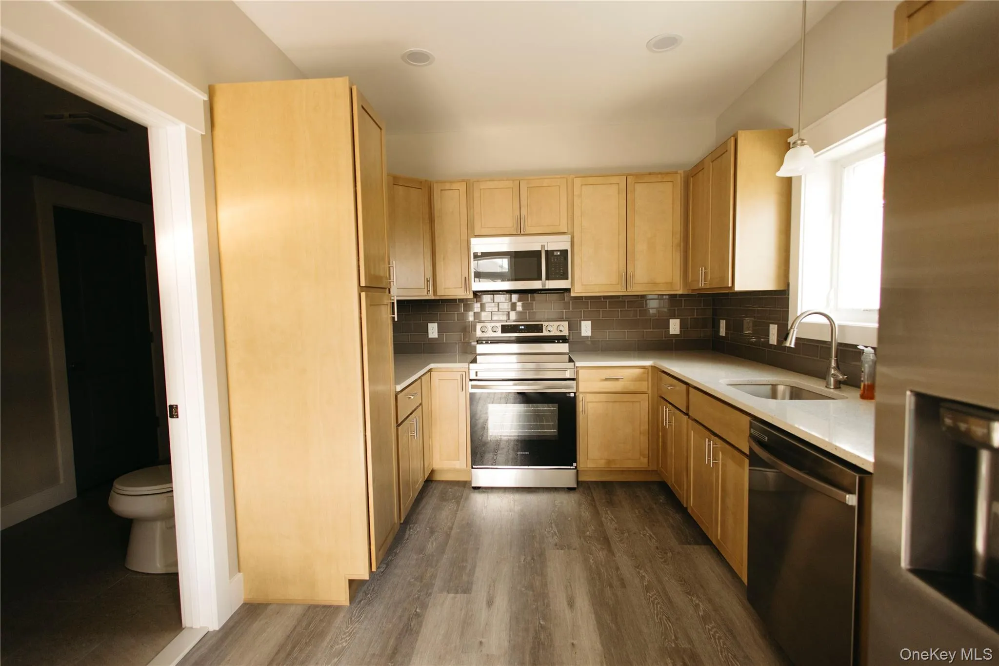 Kitchen with stainless steel appliances, light brown cabinetry, dark wood-style flooring, backsplash, and light stone counters Kitchen with stainless steel appliances, light brown cabinetry, dark wood-style flooring, backsplash, and light stone counters