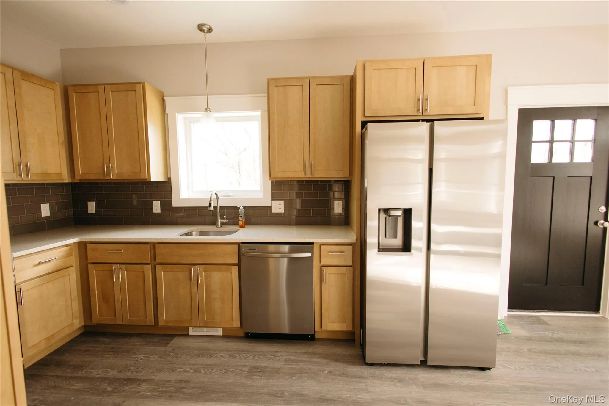Kitchen featuring stainless steel appliances, light wood finished floors, hanging light fixtures, decorative backsplash, and light brown cabinetry Kitchen featuring stainless steel appliances, light wood finished floors, hanging light fixtures, decorative backsplash, and light brown cabinetry