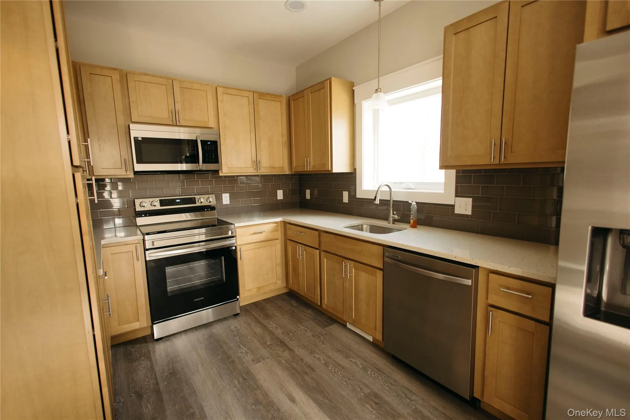 Kitchen featuring stainless steel appliances, backsplash, dark wood finished floors, and light brown cabinets Kitchen featuring stainless steel appliances, backsplash, dark wood finished floors, and light brown cabinets