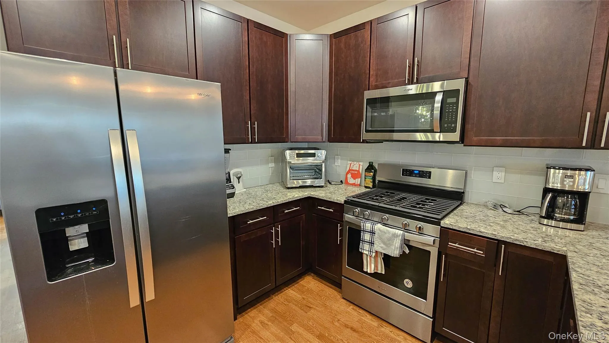 Kitchen featuring stainless steel appliances, light wood-style flooring, light stone countertops, and tasteful backsplash Kitchen featuring stainless steel appliances, light wood-style flooring, light stone countertops, and tasteful backsplash