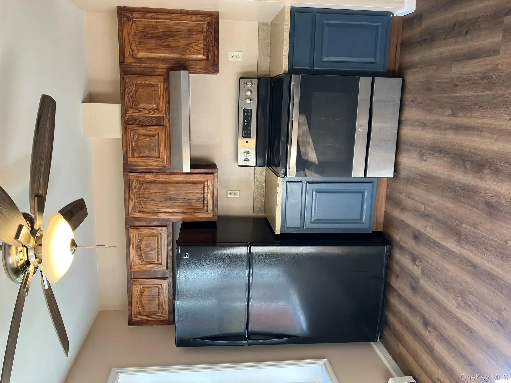 Kitchen with black stove, fridge, ceiling fan, and dark wood-style flooring Kitchen with black stove, fridge, ceiling fan, and dark wood-style flooring