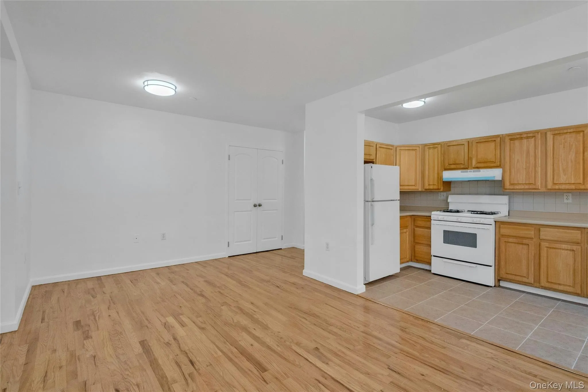 Kitchen with light countertops, white appliances, decorative backsplash, light wood-type flooring, and under cabinet range hood Kitchen with light countertops, white appliances, decorative backsplash, light wood-type flooring, and under cabinet range hood