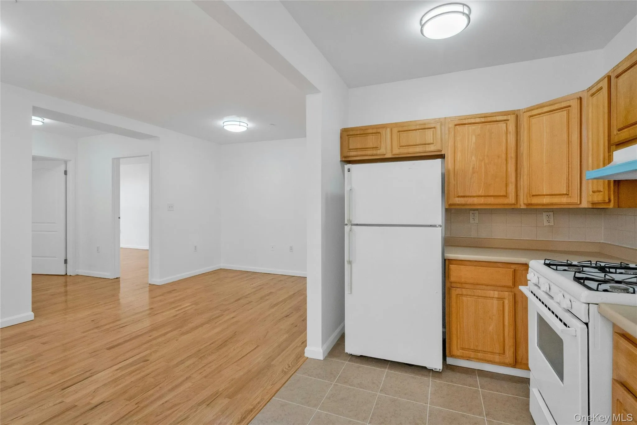 Kitchen with white appliances, light countertops, light wood-style flooring, backsplash, and under cabinet range hood Kitchen with white appliances, light countertops, light wood-style flooring, backsplash, and under cabinet range hood