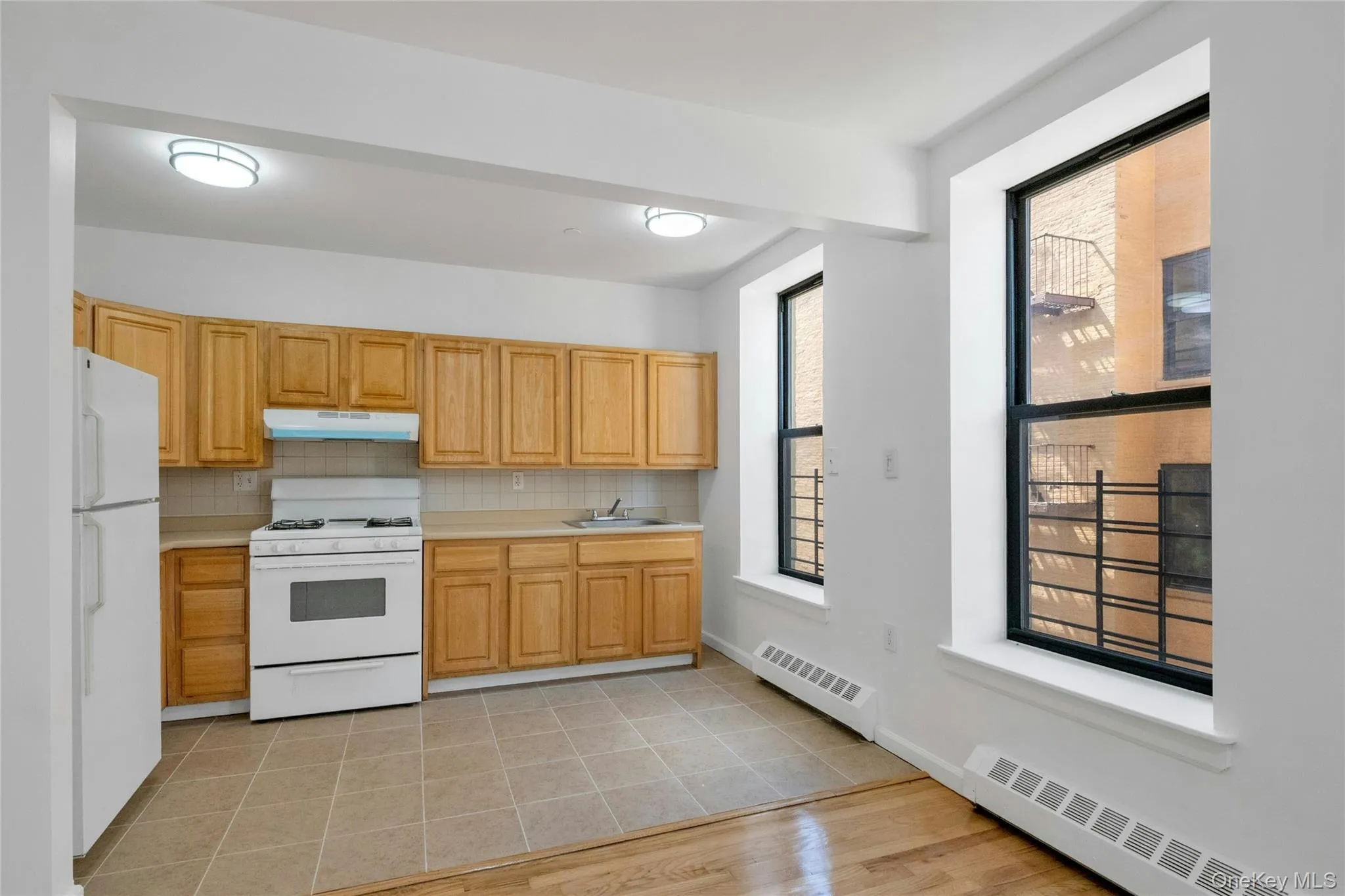 Kitchen with light countertops, white appliances, backsplash, and a baseboard radiator Kitchen with light countertops, white appliances, backsplash, and a baseboard radiator
