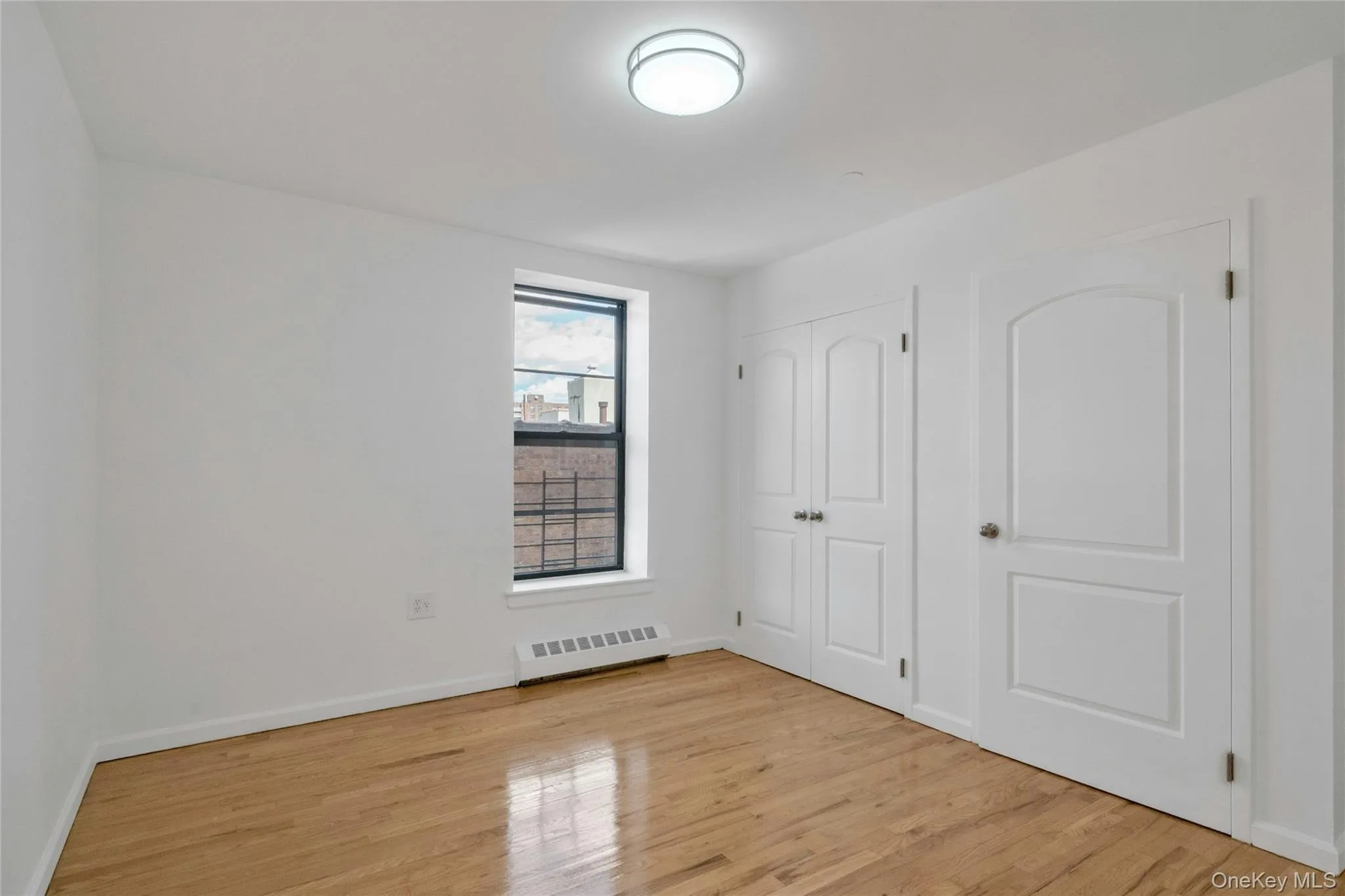 Unfurnished bedroom featuring light wood-style flooring, a closet, and a baseboard heating unit Unfurnished bedroom featuring light wood-style flooring, a closet, and a baseboard heating unit