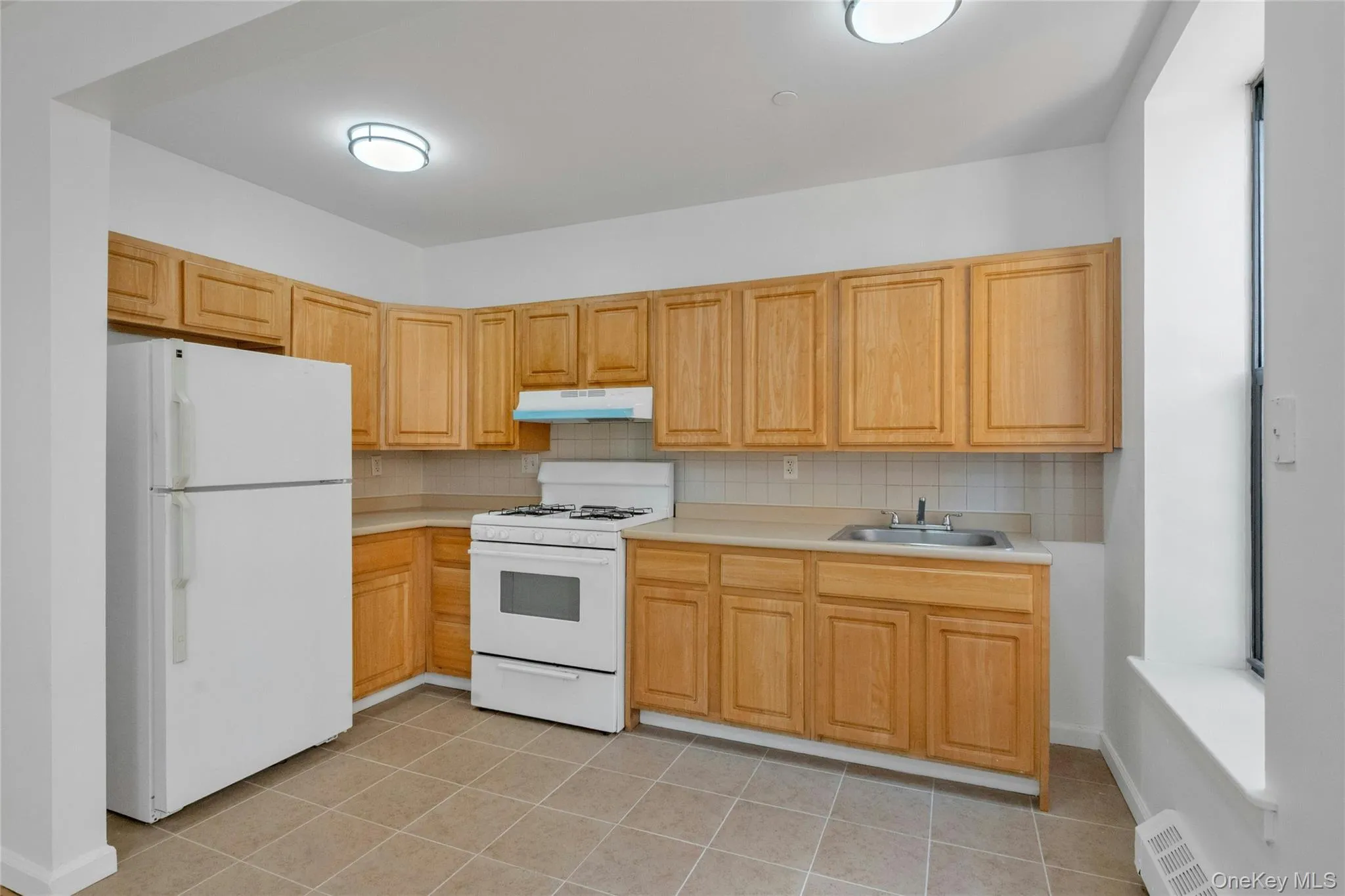 Kitchen featuring white appliances, light countertops, decorative backsplash, light tile patterned flooring, and under cabinet range hood Kitchen featuring white appliances, light countertops, decorative backsplash, light tile patterned flooring, and under cabinet range hood