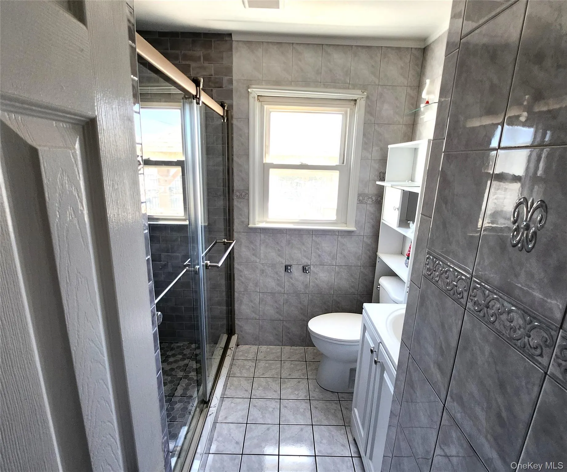 Bathroom with tile walls, light tile patterned flooring, vanity, and a shower stall Bathroom with tile walls, light tile patterned flooring, vanity, and a shower stall