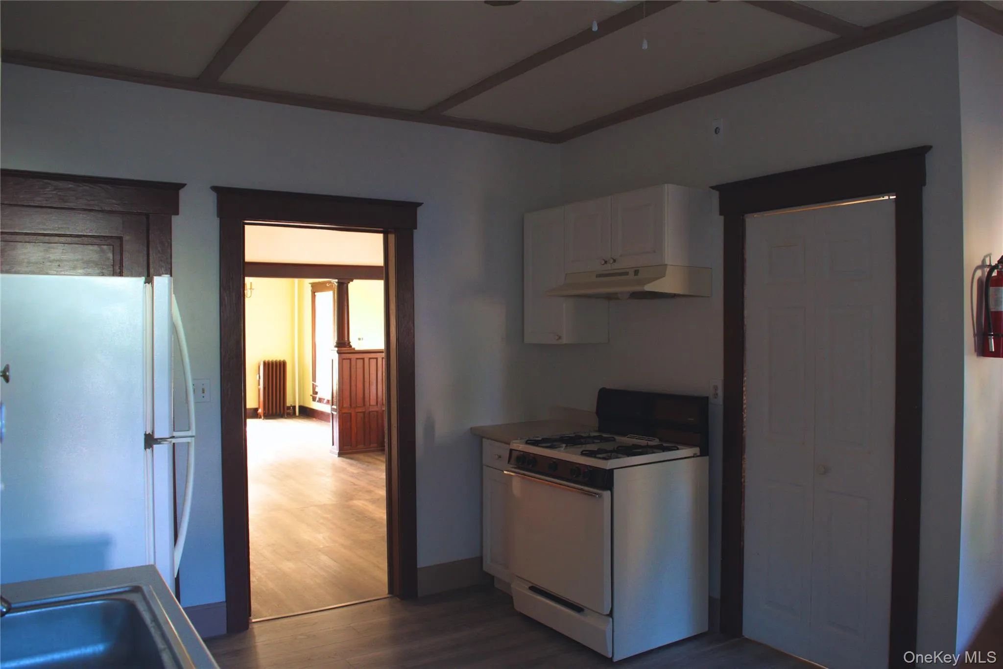 Kitchen featuring white appliances, white cabinets, dark wood finished floors, under cabinet range hood, and radiator Kitchen featuring white appliances, white cabinets, dark wood finished floors, under cabinet range hood, and radiator