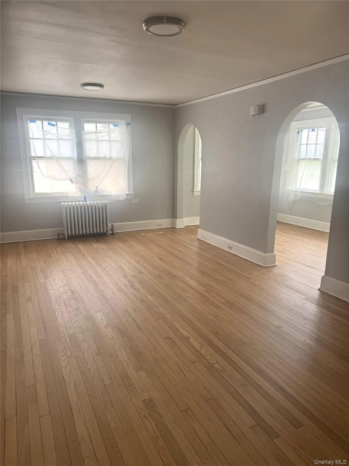 Empty room featuring light wood-style flooring, radiator, arched walkways, and ornamental molding Empty room featuring light wood-style flooring, radiator, arched walkways, and ornamental molding