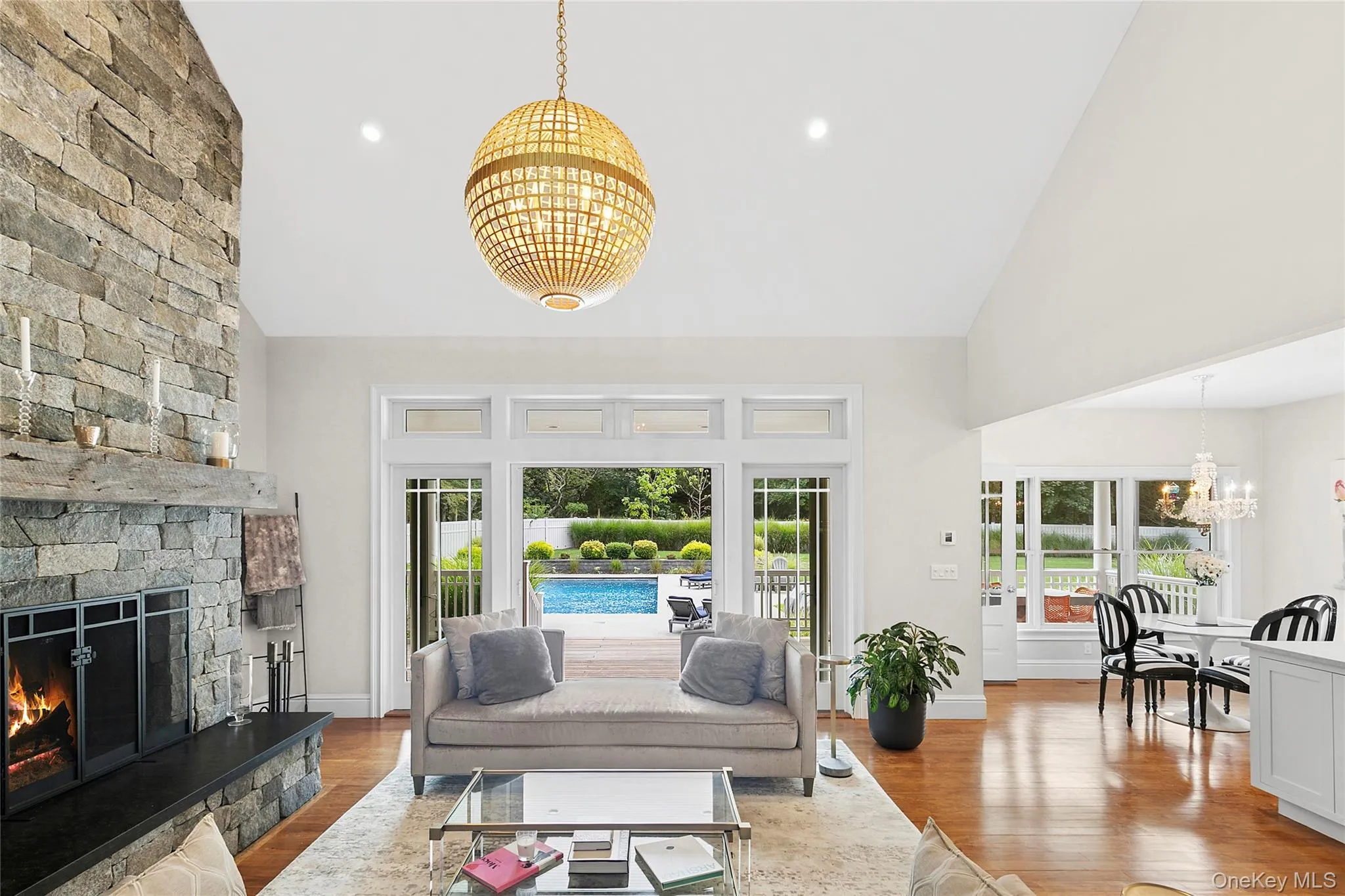 Living room featuring a chandelier, light wood-style flooring, high vaulted ceiling, a fireplace, and recessed lighting Living room featuring a chandelier, light wood-style flooring, high vaulted ceiling, a fireplace, and recessed lighting