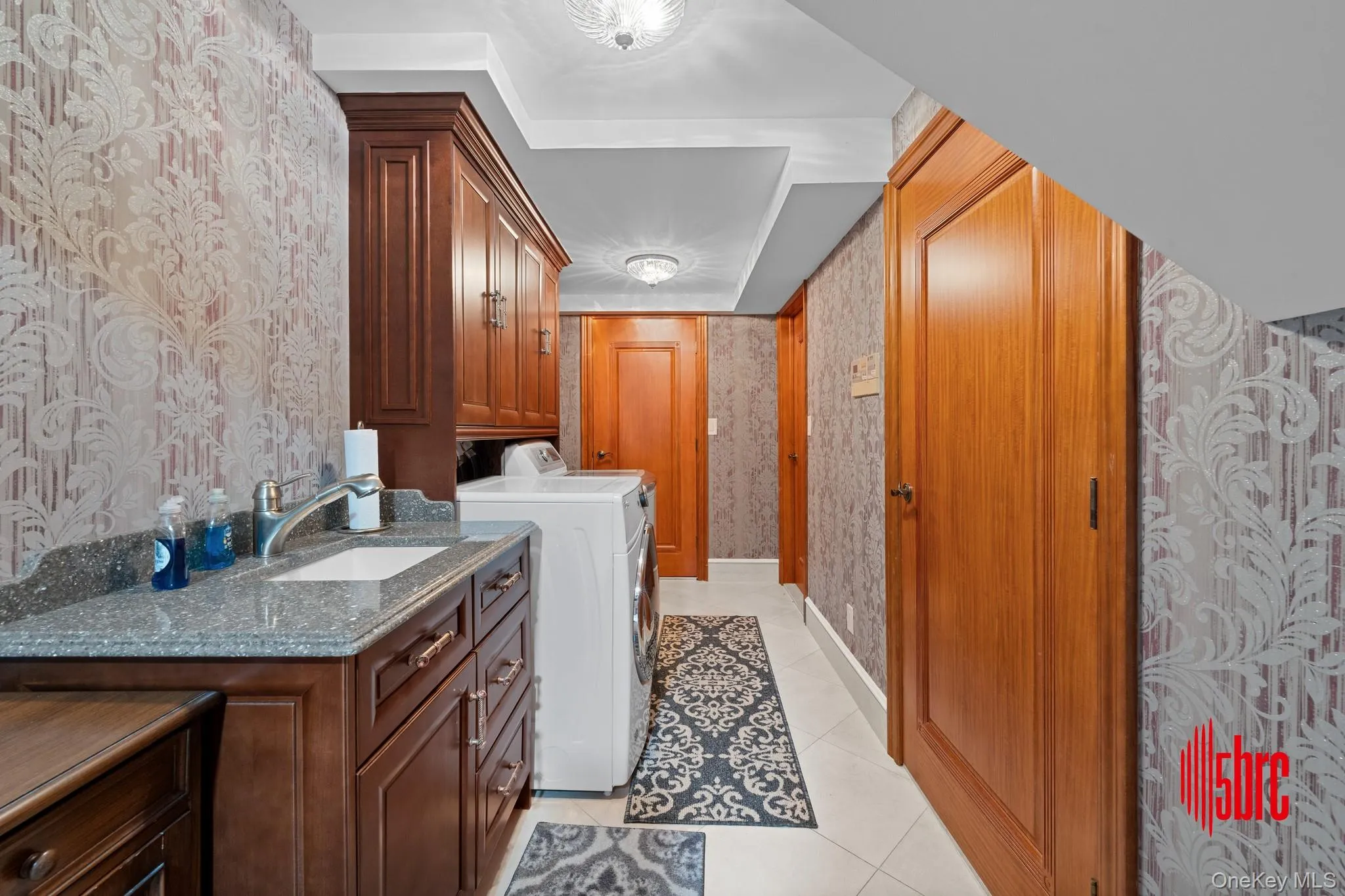 Washroom featuring wallpapered walls, independent washer and dryer, light tile patterned flooring, and cabinet space Washroom featuring wallpapered walls, independent washer and dryer, light tile patterned flooring, and cabinet space