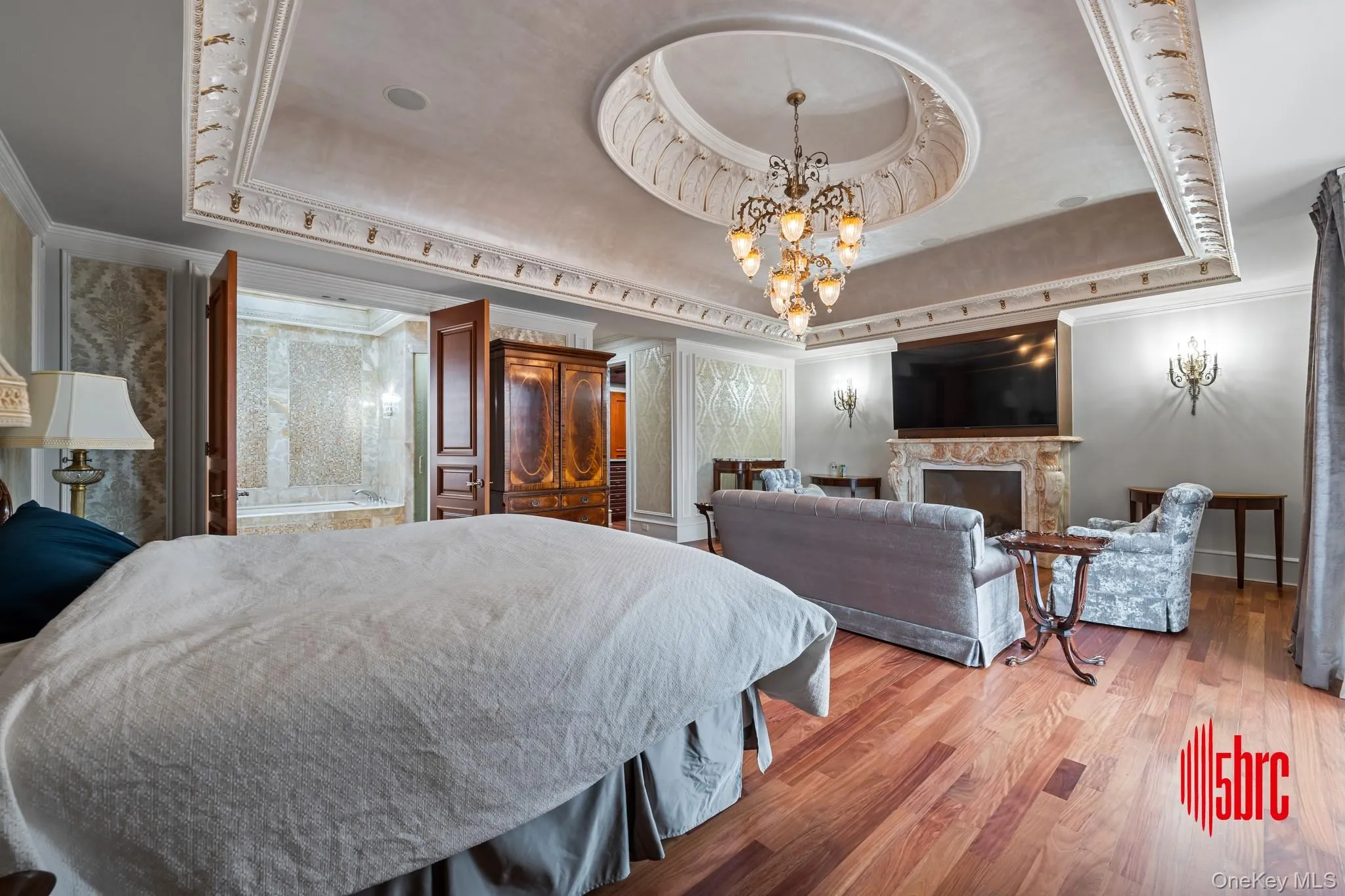 Bedroom featuring a tray ceiling, crown molding, a premium fireplace, wood finished floors, and a chandelier Bedroom featuring a tray ceiling, crown molding, a premium fireplace, wood finished floors, and a chandelier